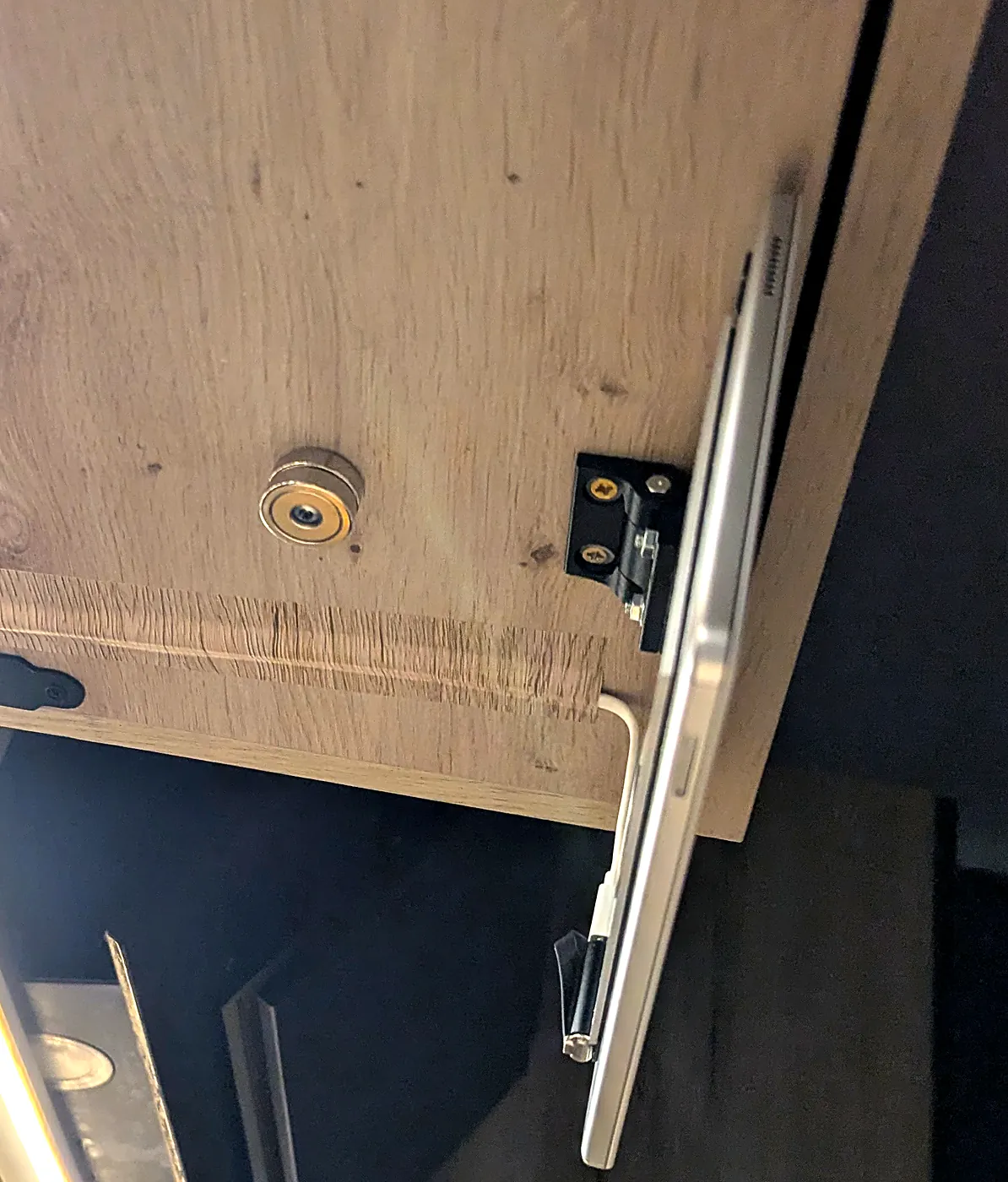 Cabinet floor from below: stacked pot magnets, hinge at the front edge, tablet hanging vertically, white cable at the hinge edge